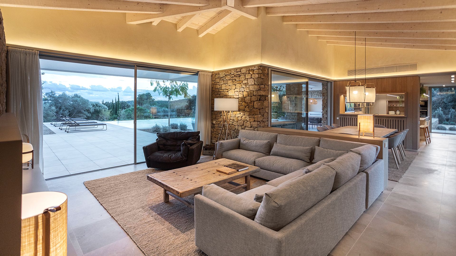 Salón comedor con salida a la piscina, techo de madera, sofá gris, alfombra gris, mesa de centro de madera lámparas de techo y de pie
