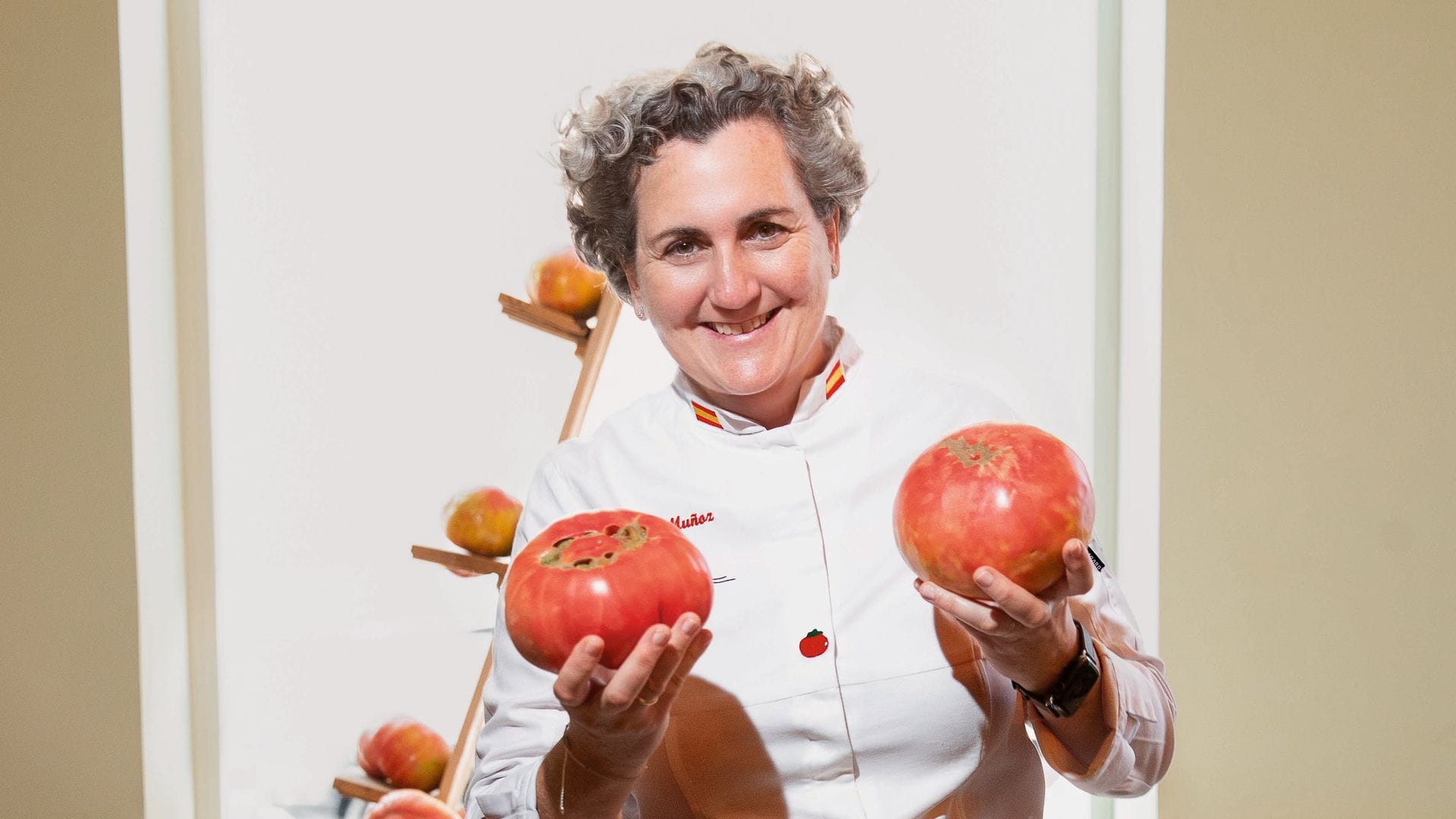 Pepa Muñoz con uniforme blanco sostiene dos manzanas rojas en una cocina.