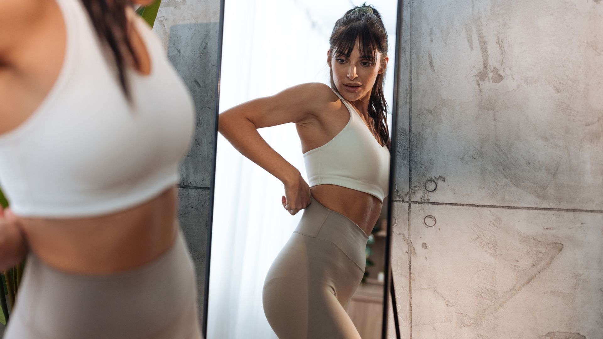 Mujer joven morena con conjunto deportivo y coleta alta mirándose en el espejo