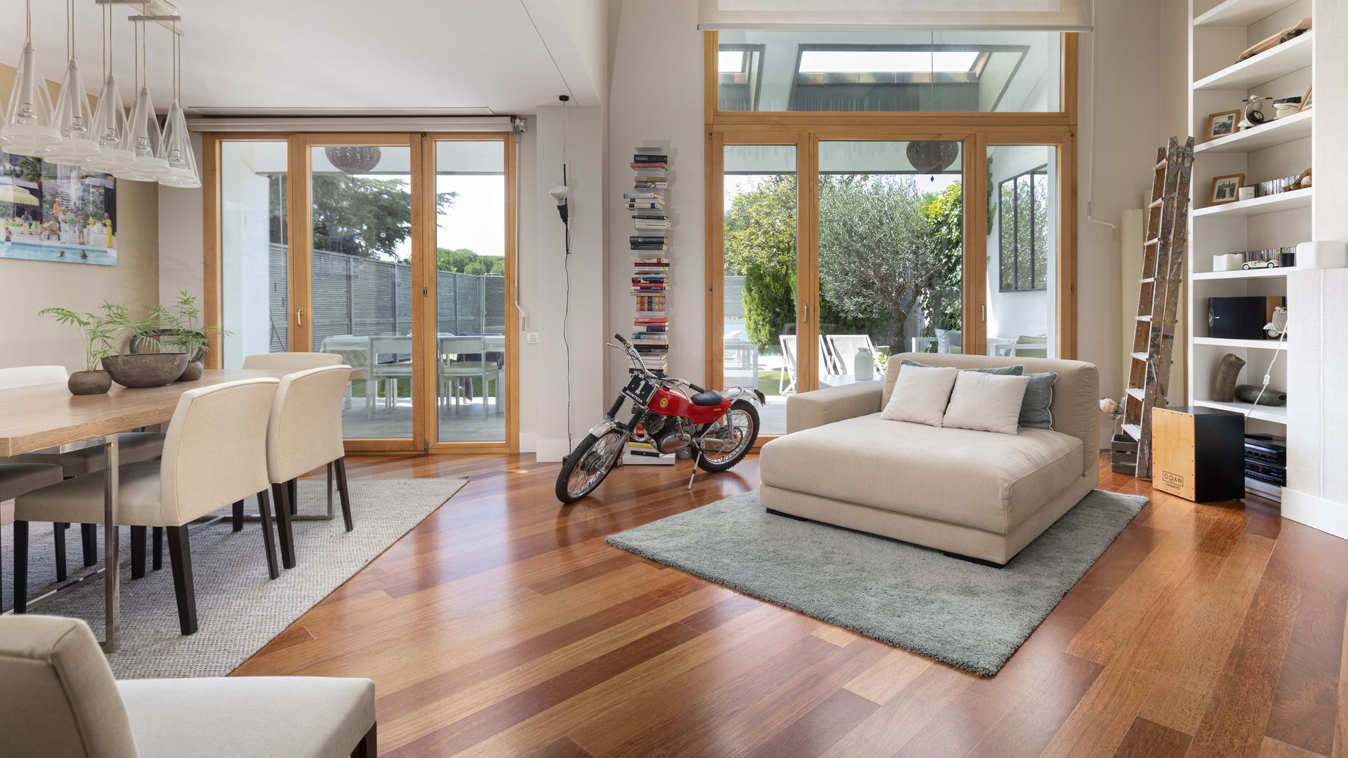 Salón comedor con rincón con sofá en modo cama, junto a una librería, una moto, una alfombra, salida al jardín