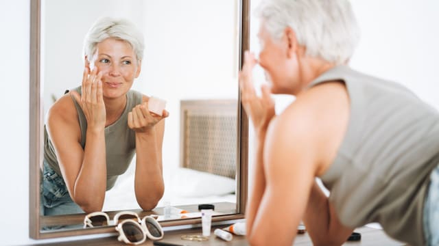 Mujer de pelo blanco frente al espejo aplicándose crema facial