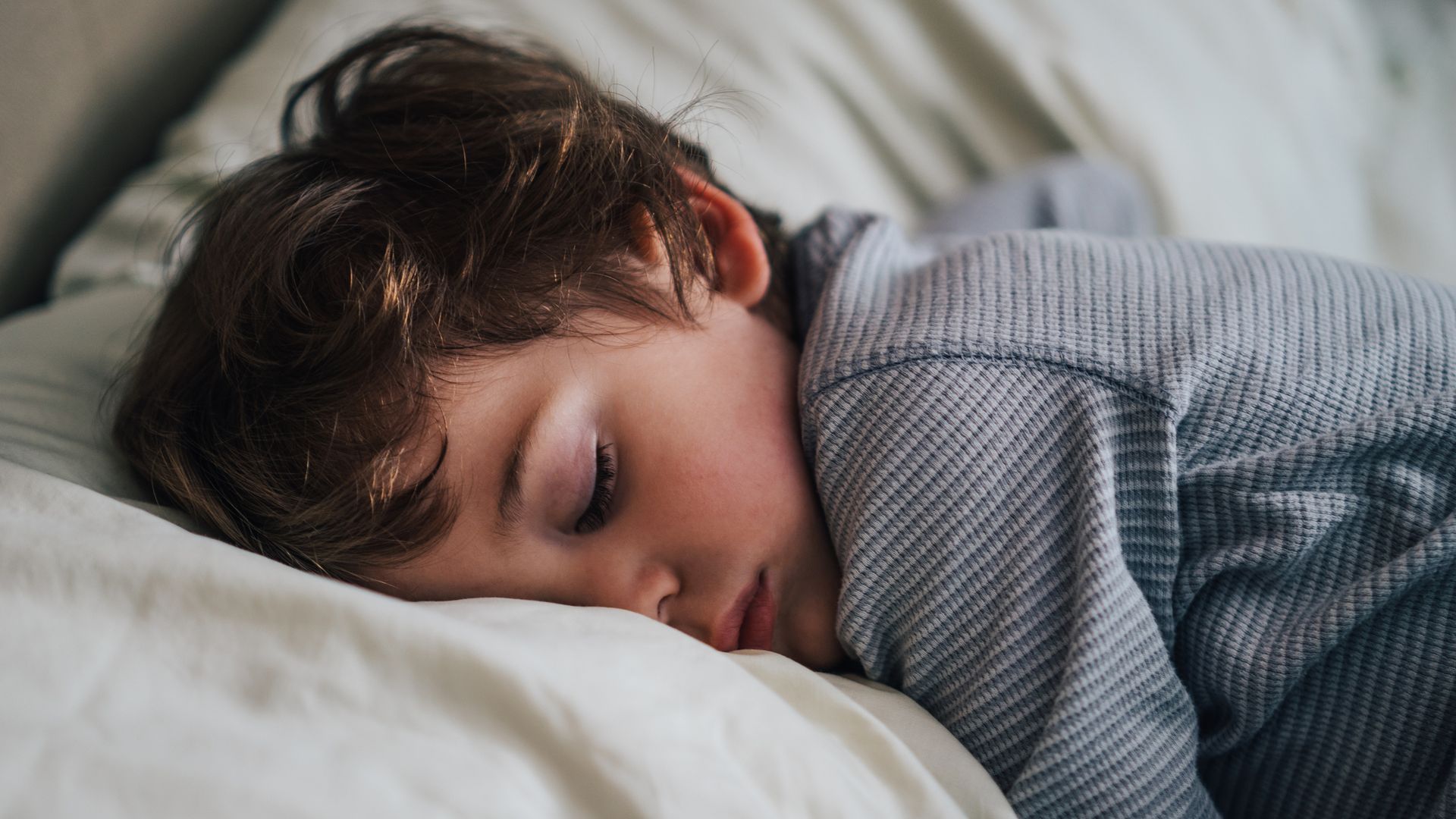 Niño pequeño durmiendo profundamente sobre una almohada blanca, boca abajo con un pijama azul.