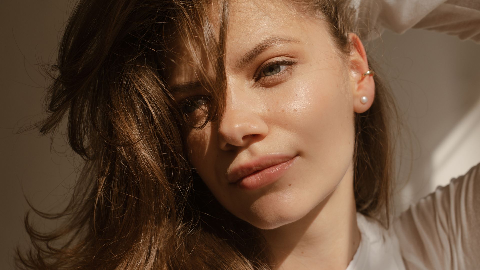 Rostro de mujer con piel lisa y luminosa, sujetándose el pelo con una mano