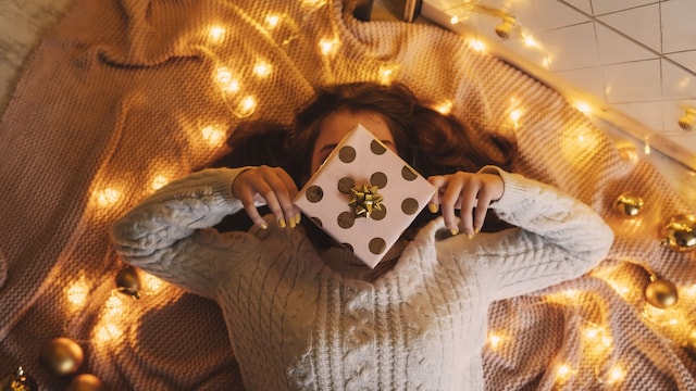 Mujer tumbada en el suelo sobre una manta con un regalo de Navidad y luces en dorado