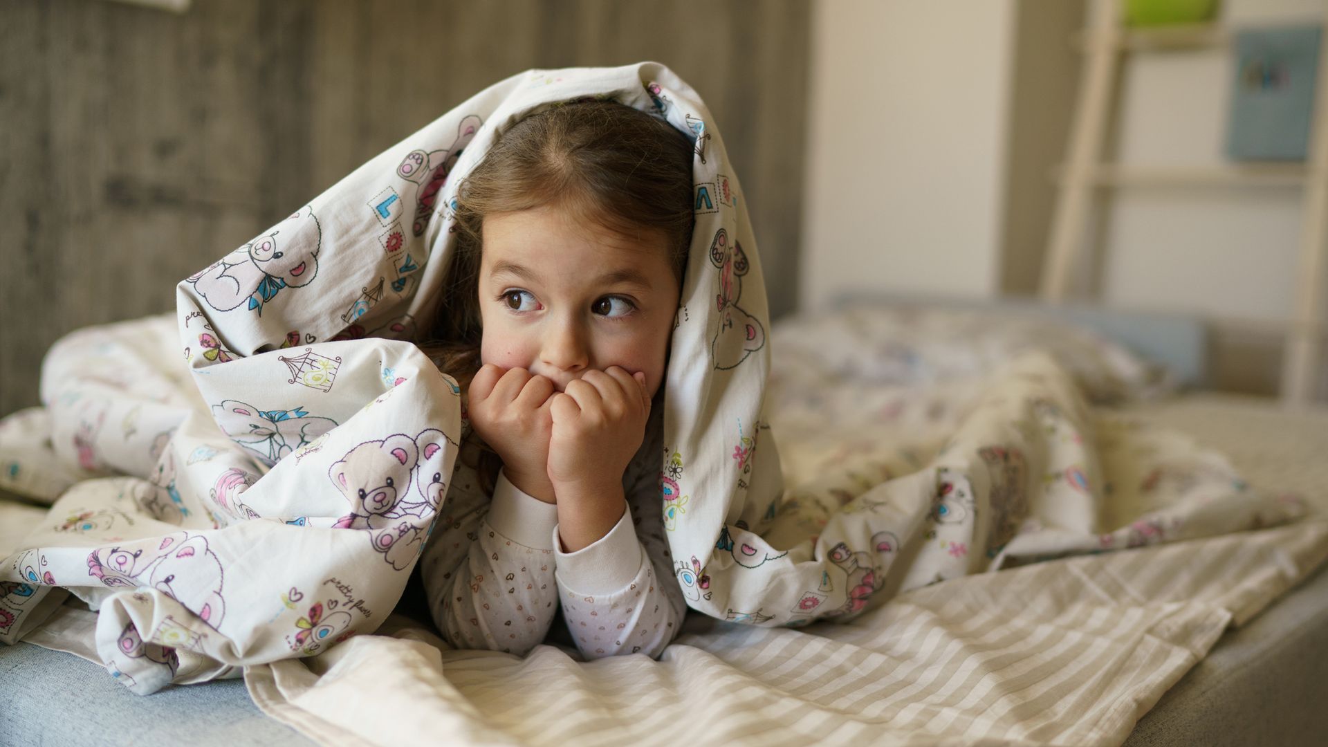 niña asustada tapada con una sábana en la cama
