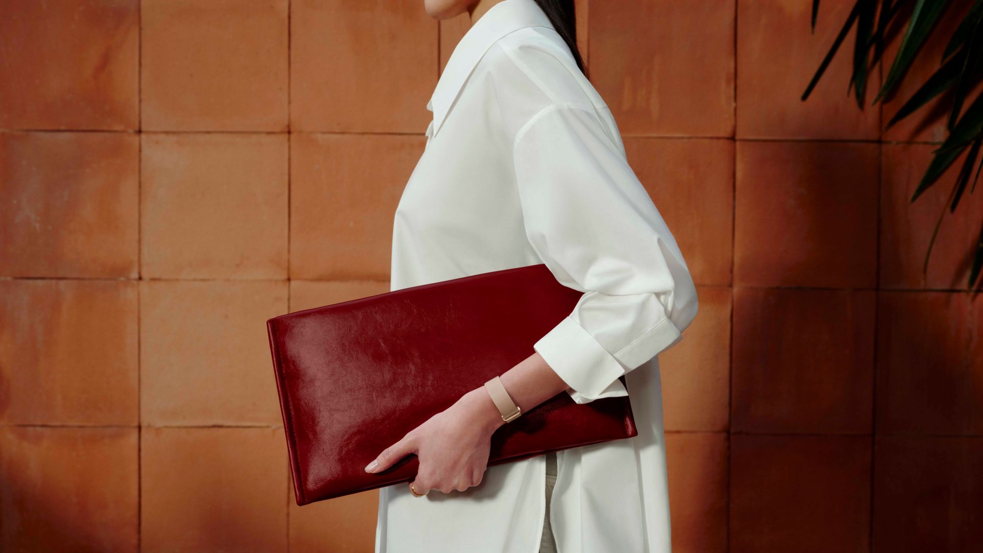Mujer con la Google Fitbit Air sujetando una cartera de mano granate, con ropa formal: blusa blanca y pantalones en 'beige'.