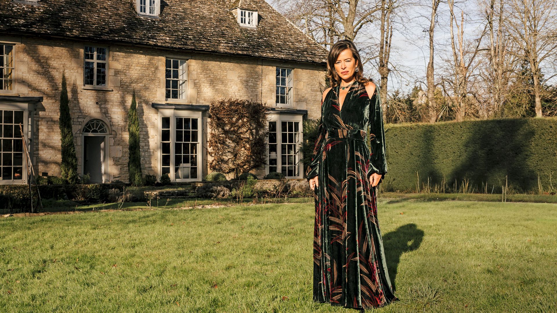 Jade Jagger en vestido largo, posando en césped frente a casa antigua.