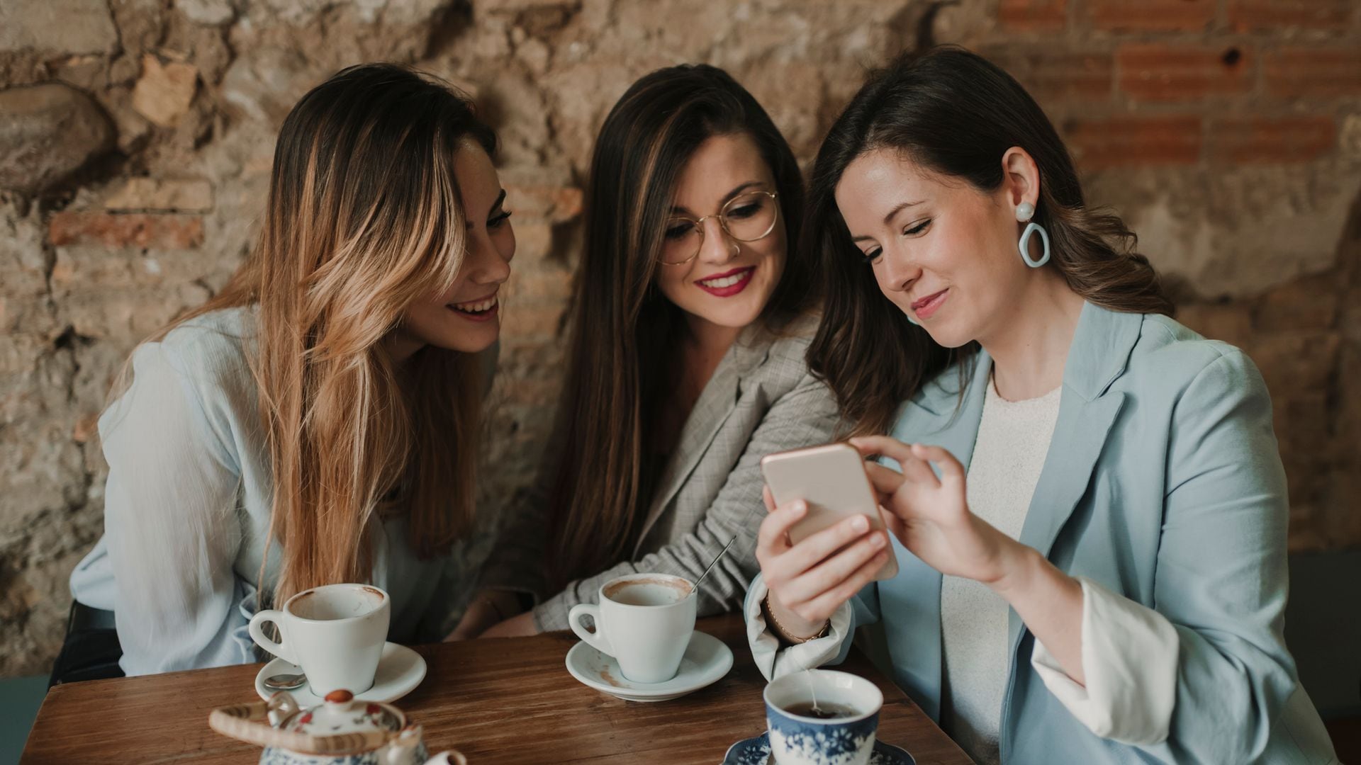 Tres mujeres trabajadoras mirando el teléfono mientras toman café