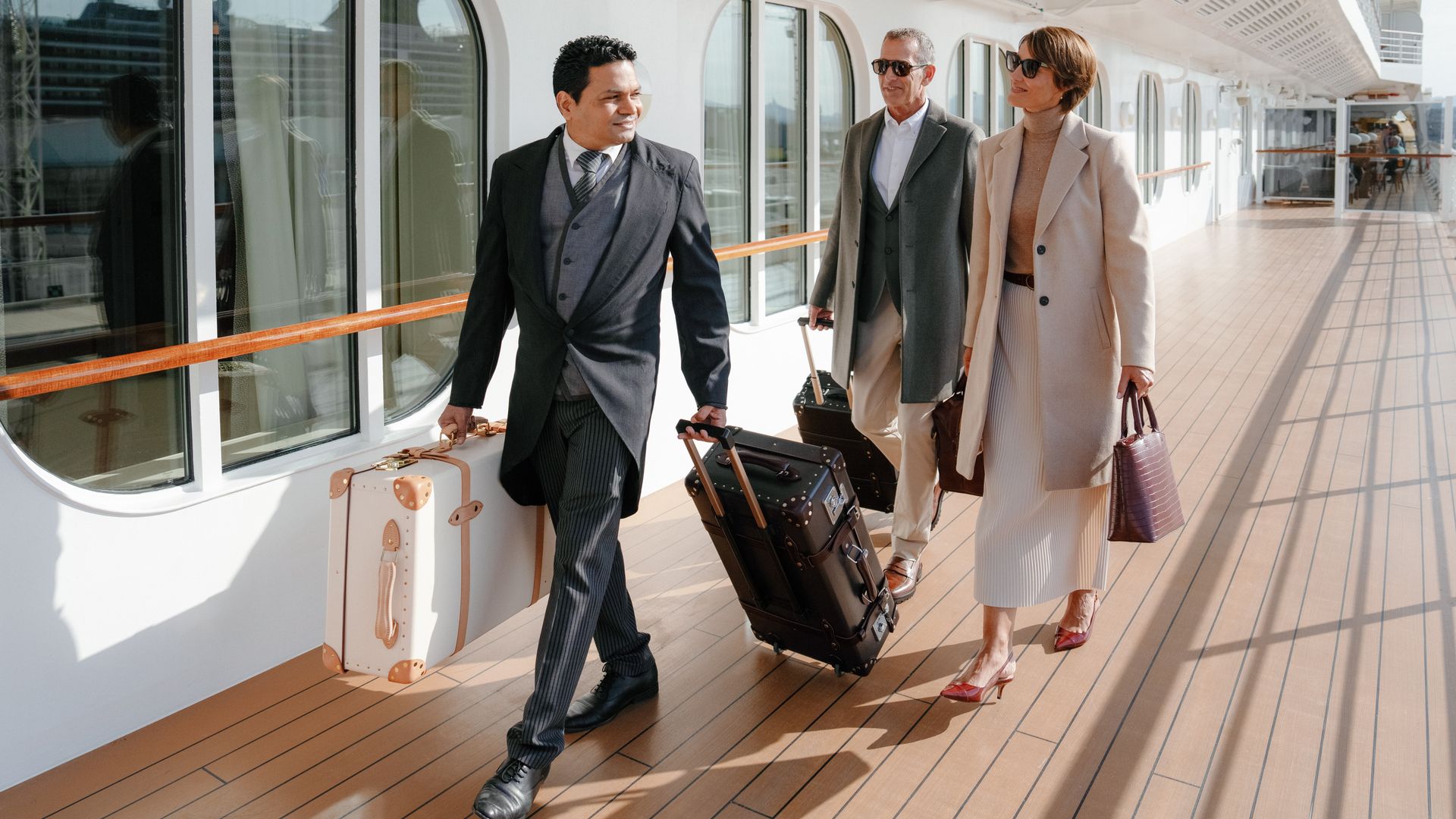 Personal ayudando con las maletas a una pareja en cubierta de uno de los cruceros Regent Seven Seas Cruises® 8.