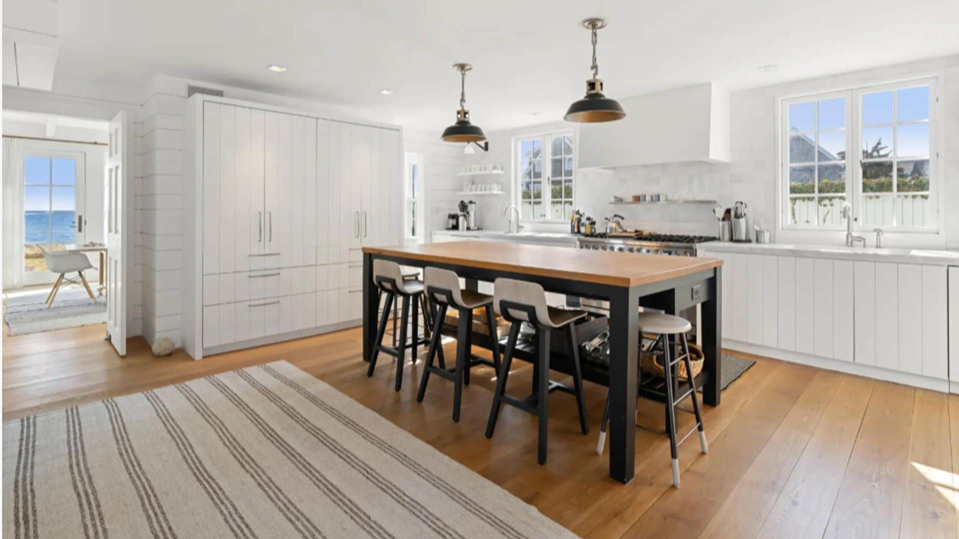 Casa Taylor Swift cocina blanca con isla de madera, suelo de madera, ventanas, armarios, lámparas de techo