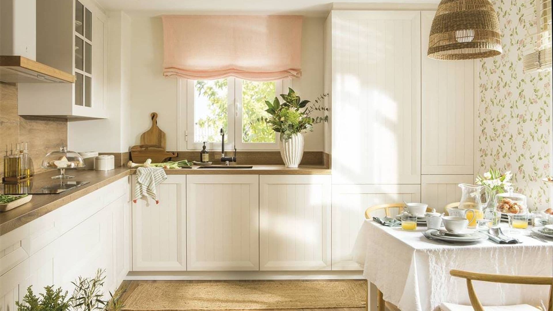 Cocina con comedor, de estilo cottage, con papel pintado de flores, muebles blancos, estor, lámpara de techo de fibras vegetales, solo de madera, mesa con mantel y servicio de desayuno