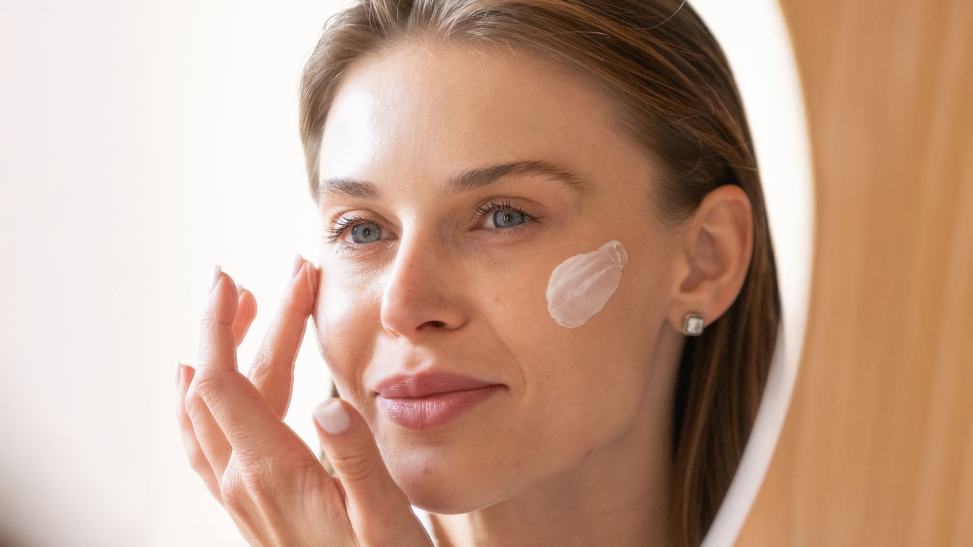 Rostro de mujer aplicándose crema en la cara mientras se mira al espejo