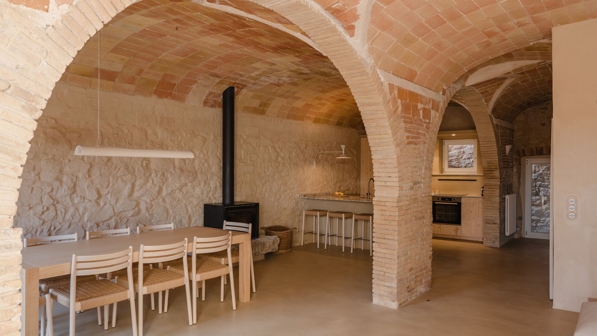 Cocina abierta al comedor con bóvedas, paredes de piedra, mesa de comedor de madera, estufa de leña negra 