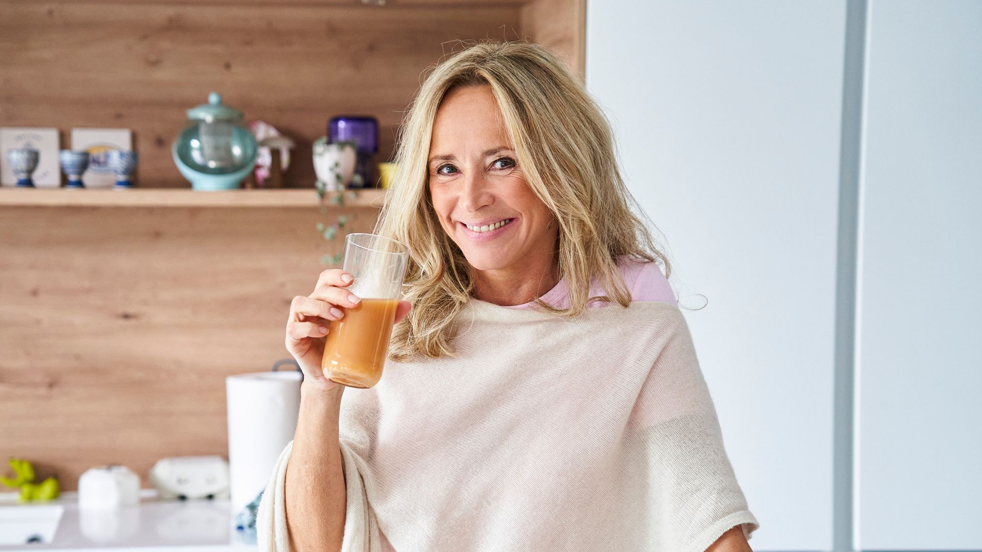 Una mujer rubia tomando un batido de frutas en la cocina