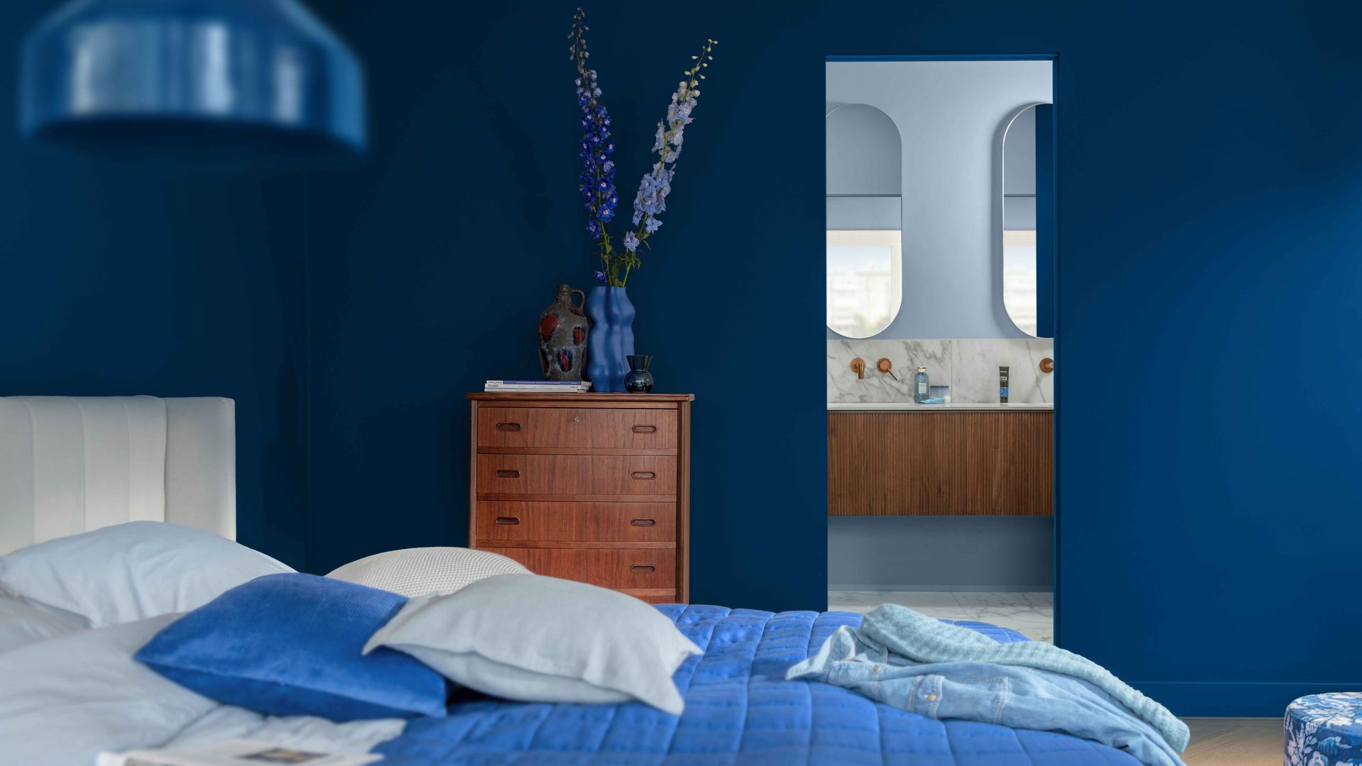 Dormitorio con baño con paredes en azul Klein, ropa de cama azul más claro y paredes baño en azul cielo, cómoda de madera