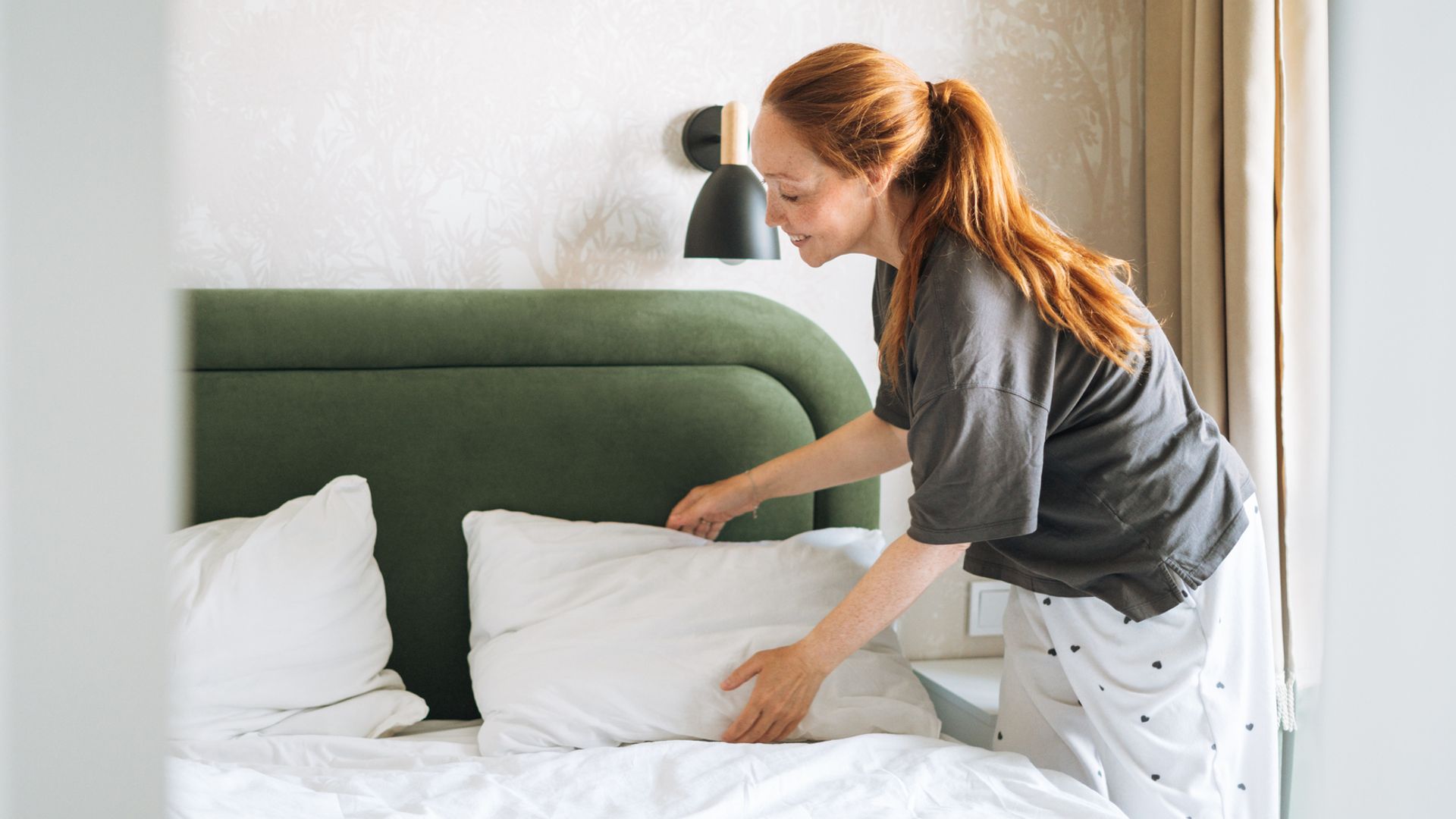 Chica haciendo la cama en pijama. Una cama blanca, con cabecero verde.