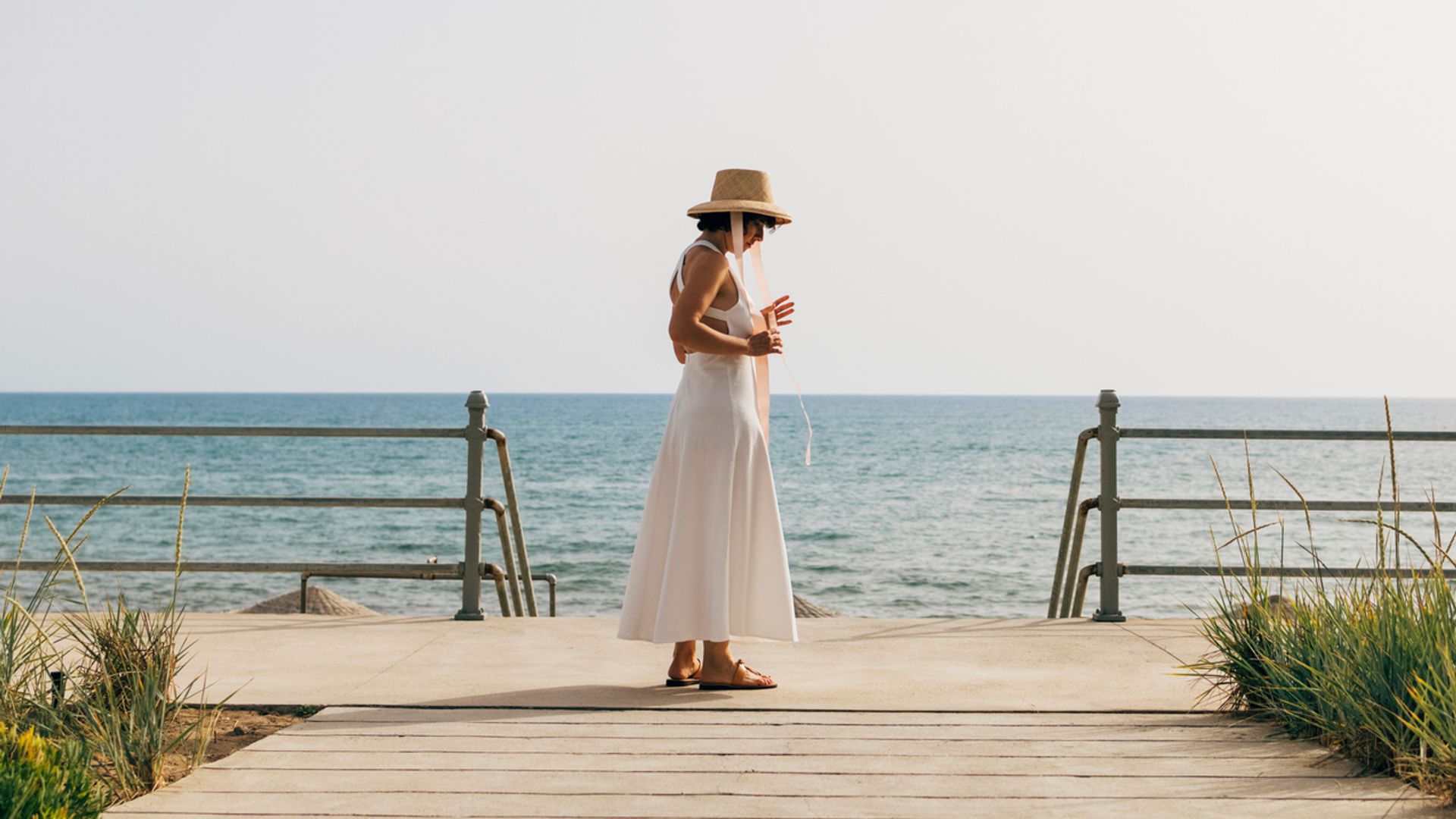 Mujer con vestido blanco y sombrero de rafia frente al mar