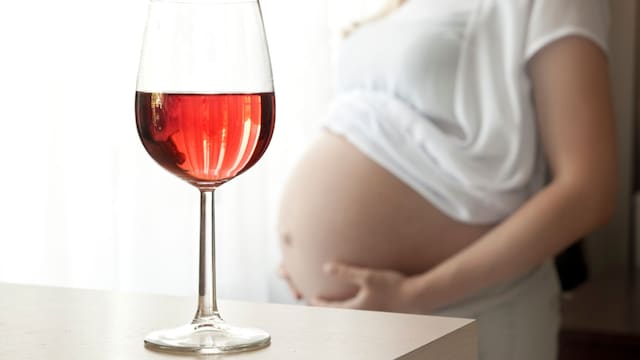 Copa de vino en primer plano con embarazada al fondo