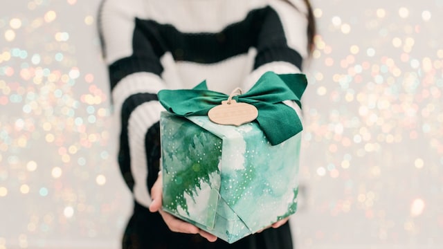 Mujer sujetando un regalo envuelto por Navidad con fondo brillante en blanco