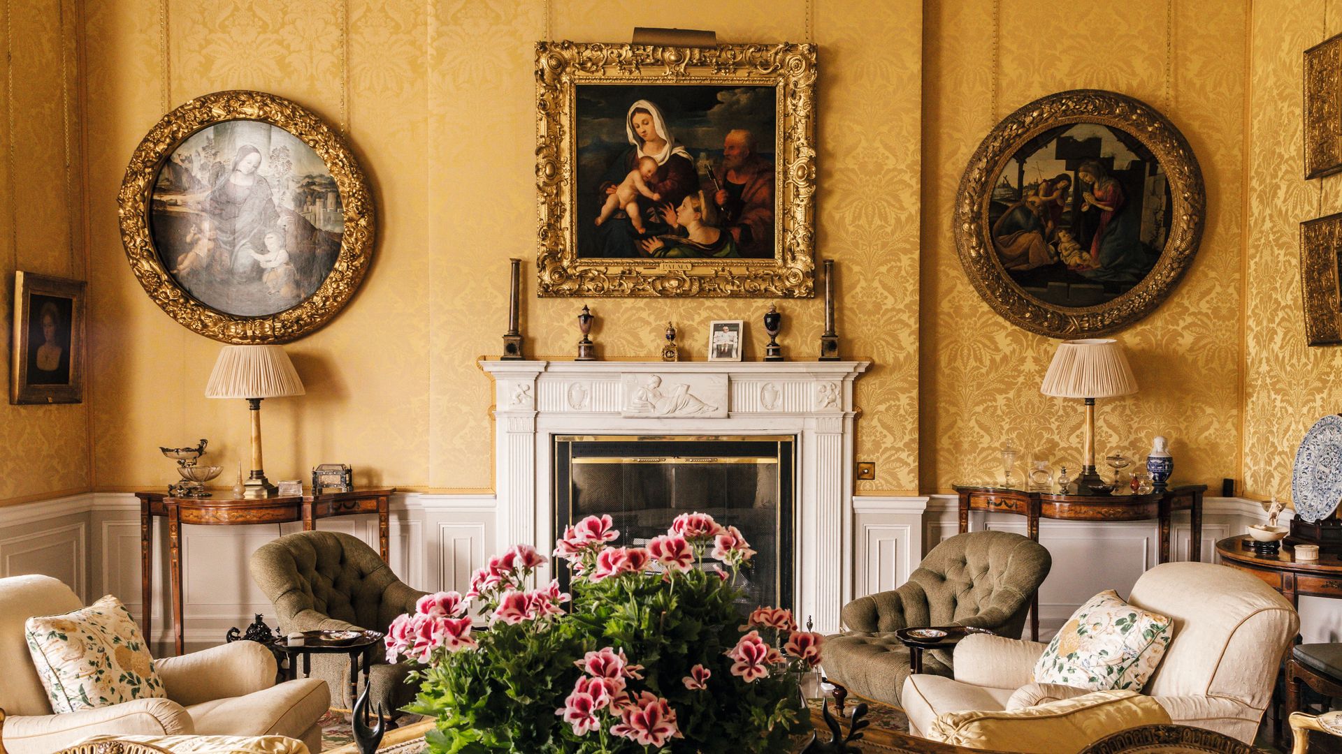Sala de estar elegante con sofás, flores, chimenea y cuadros en las paredes.