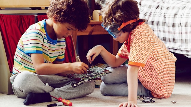 Dos niños jugando en el suelo de su habitación con un juguete de electrónica.