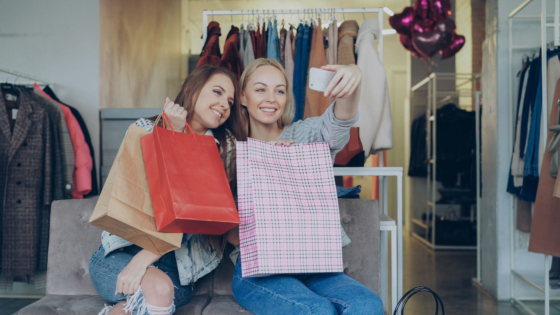 Dos chicas haciéndose un 'selfie' con el teléfono móvil enseñando sus compras en una tienda.