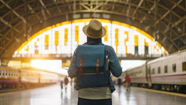 Joven con una mochila de viaje a su espalda en el centro del andén de una estación de tren