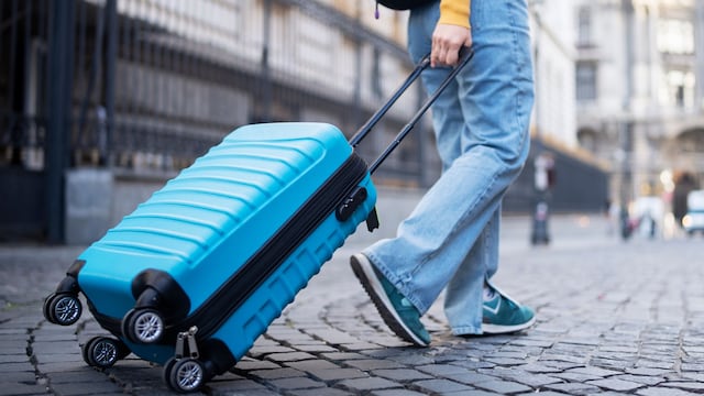 Turista viajando con la maleta en primavera por una calle empedrada con una maleta de cabina azul