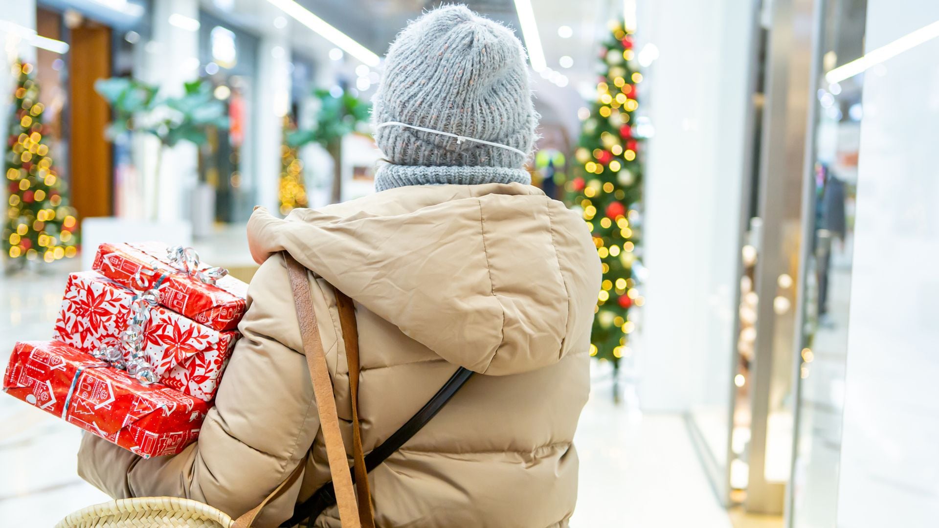 Mujer comprando regalos de Navidad en unos grandes almacenes con paquetes envueltos en una mano.