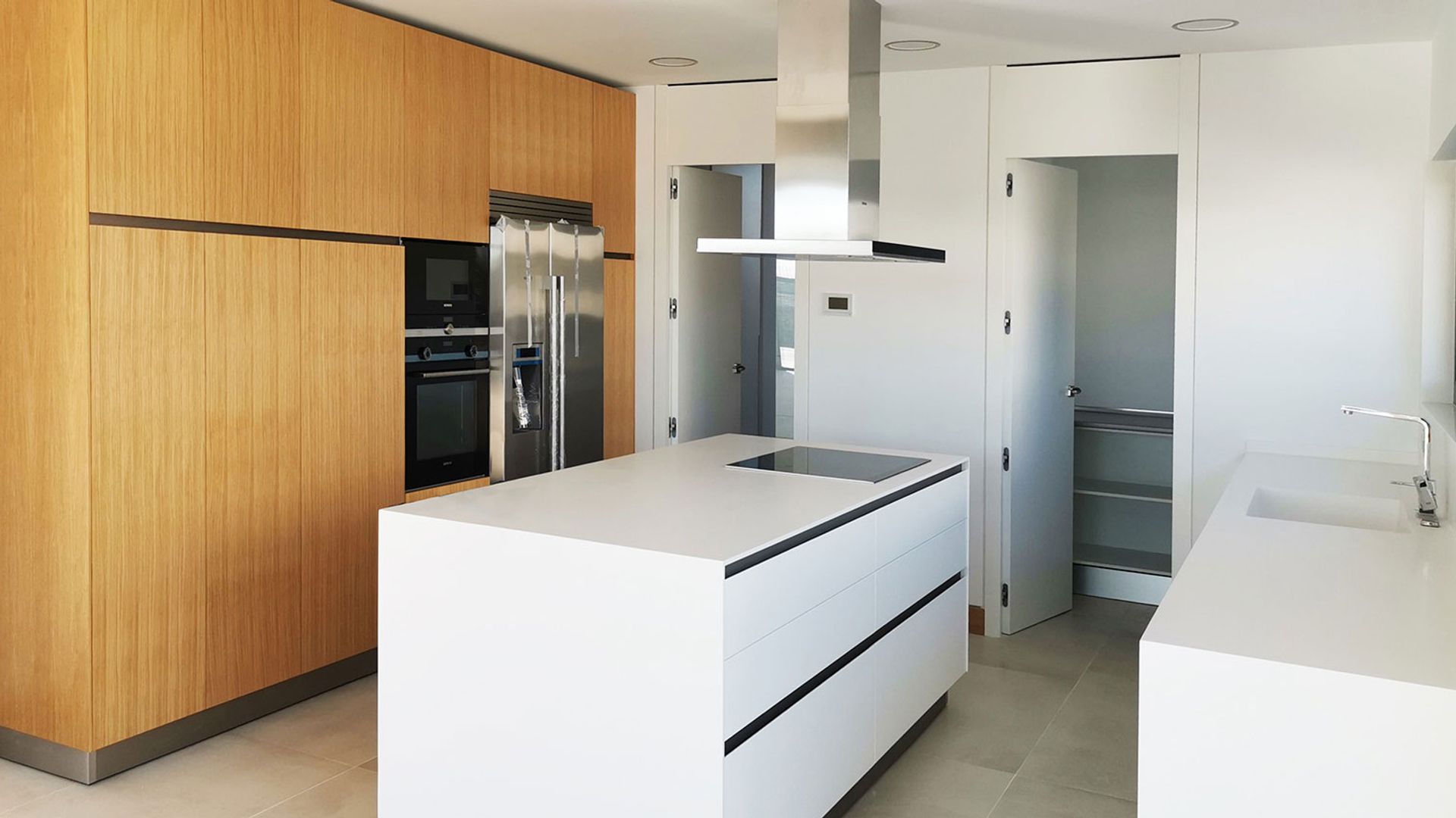 Cocina blanca con isla central, despensa, módulo de armarios en madera y campana de techo