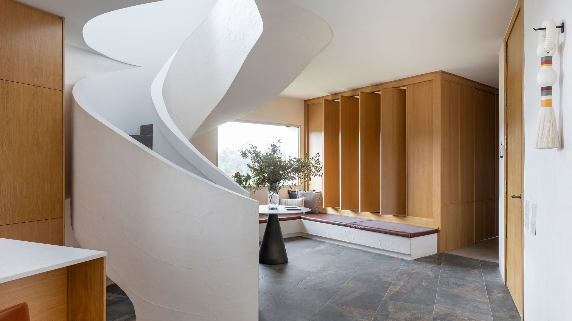 Entrada con escalera escultura, banco de obra, paneles de madera, suelo porcelánico