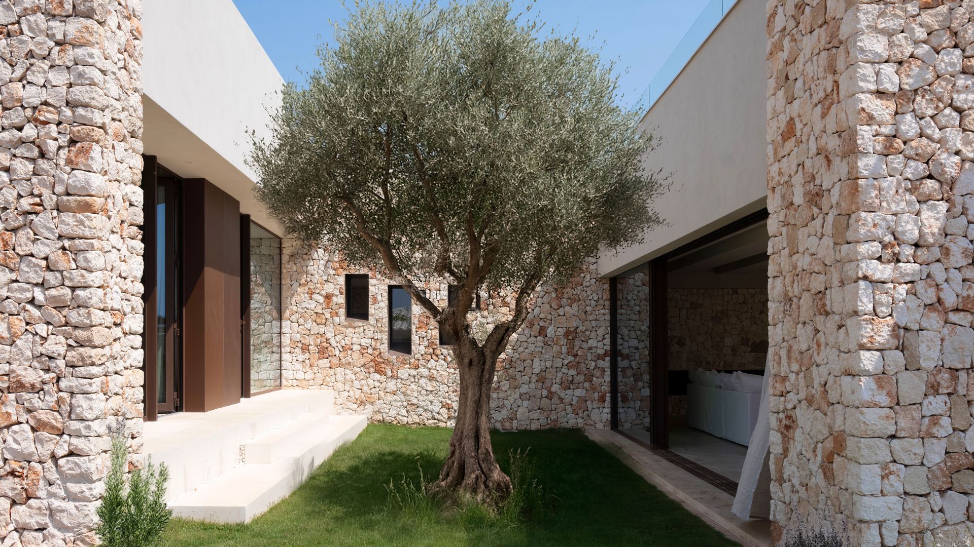 Casa de piedra con un olivo en el centro, césped