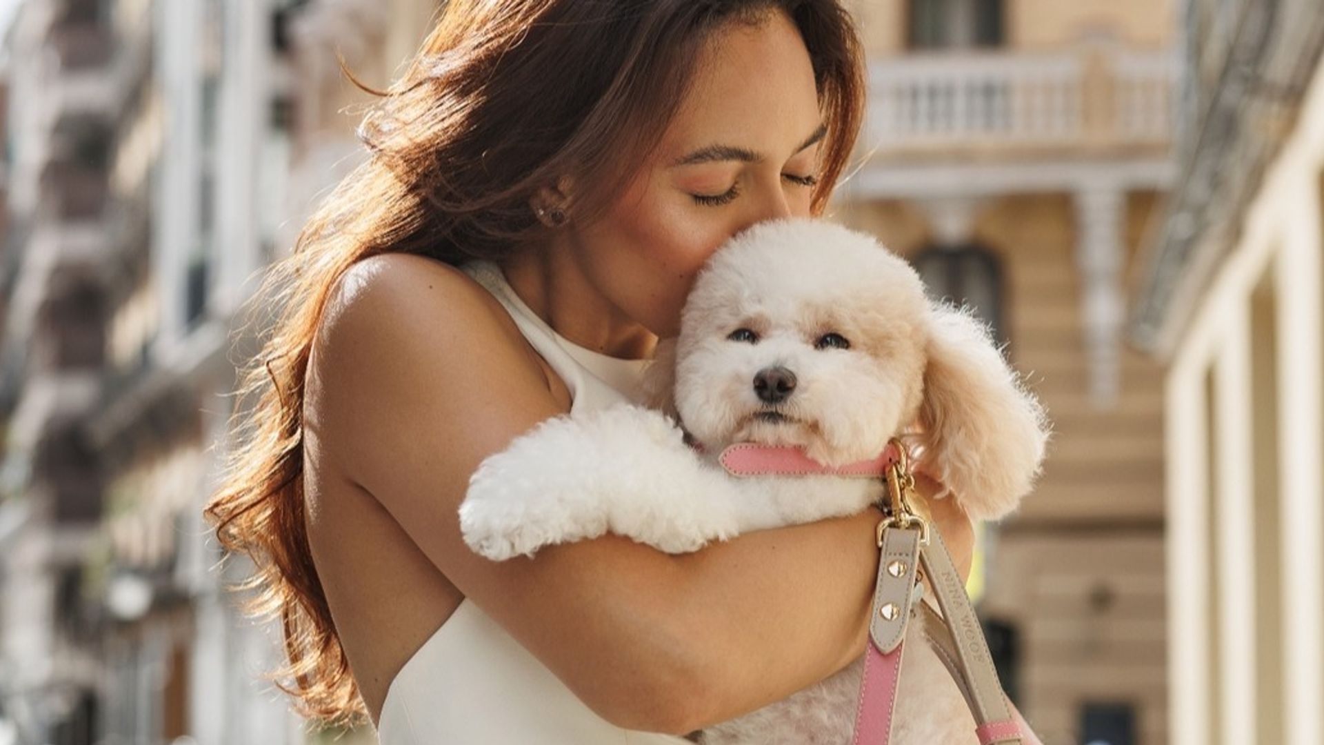 Mujer morena con vestido blanco besando a su perrito caniche en brazos
