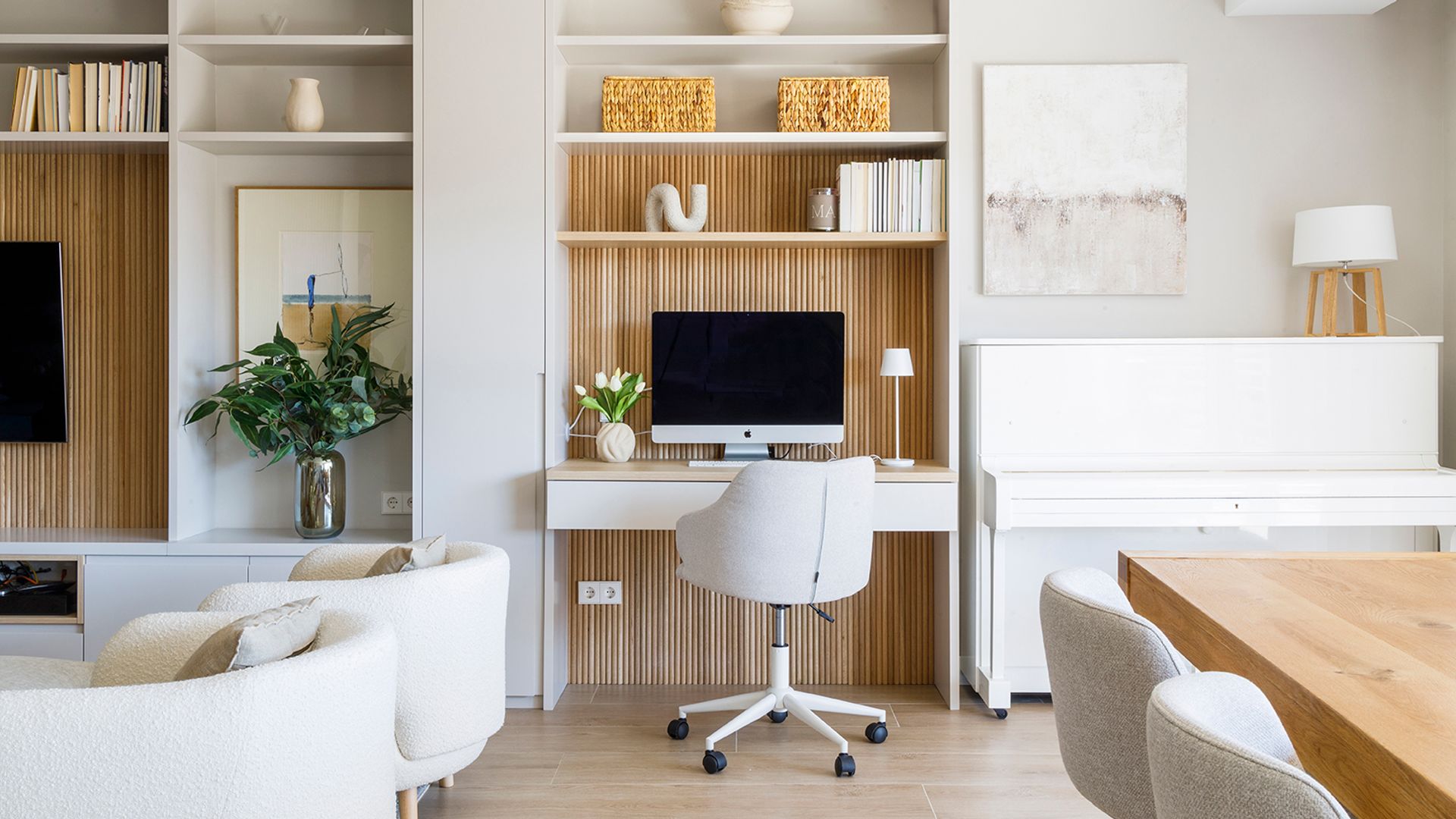 Salón comedor con despacho en la estantería a medida, piano, mesa de madera, butacas blancas, sillas tapizadas 