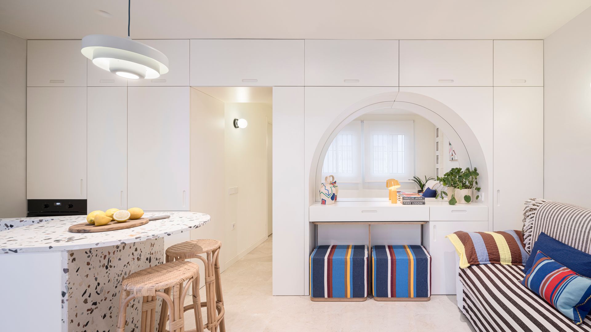 Salón con isla de cocina, estructura a medida de suelo a techo, con tocador con pufs, sofá con tela de rayas