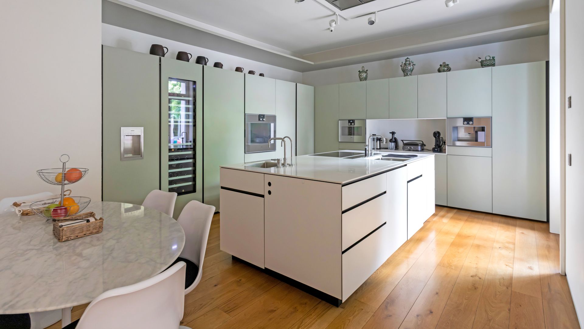Cocina con isla y office con mesa de comedor redonda, muebles de color verde claro