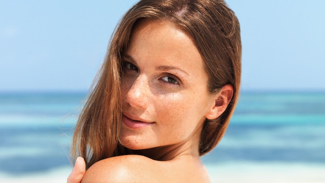 Rostro de mujer con cabello castaño junto a la playa