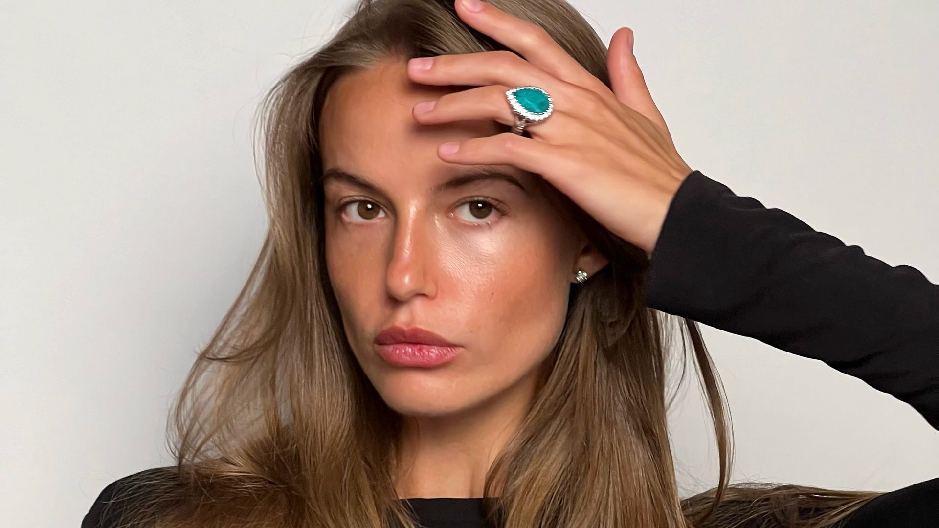 Primer plano de la modelo Alyona Lozovaya con pelo suelto, jersey negro y anillo turquesa en el dedo