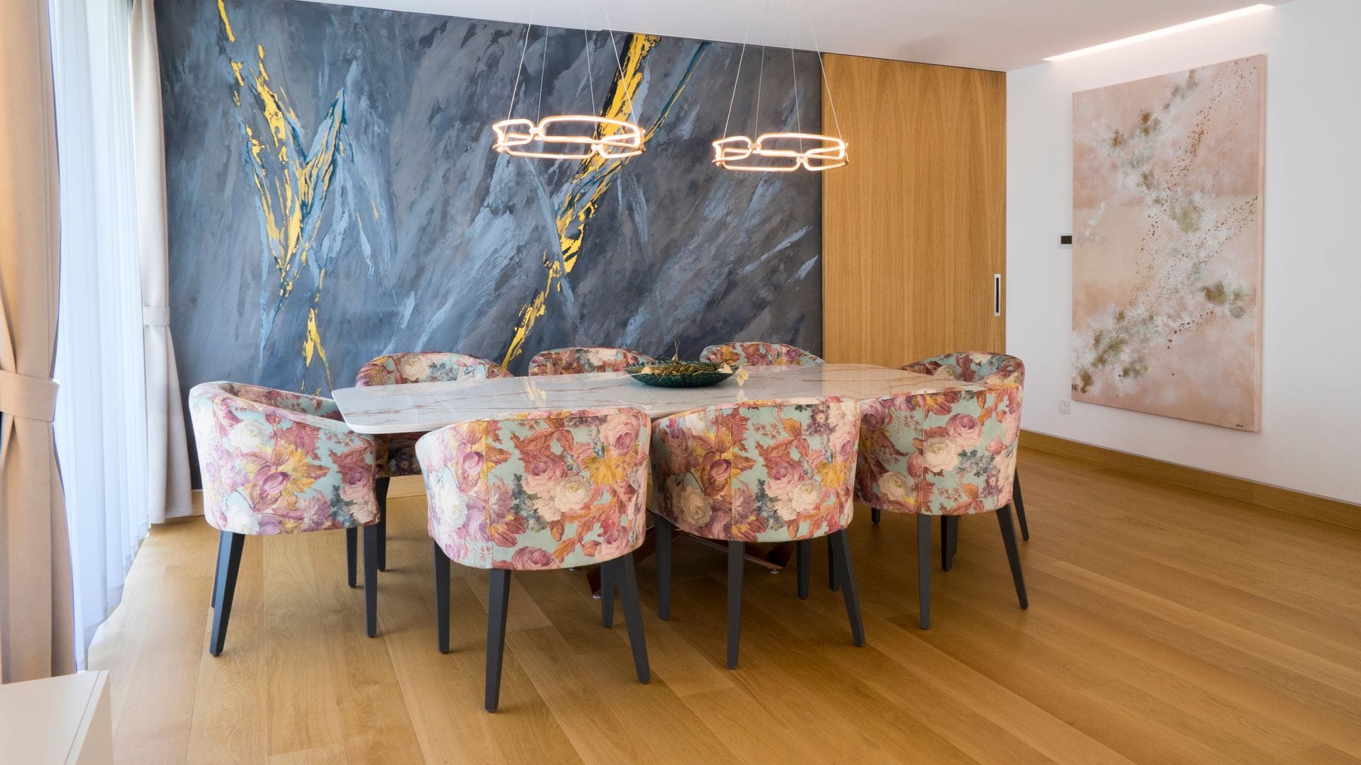 Comedor con mesa rectangular, gran mural en tonos azules, lámparas de techo, cuadro y puerta corredera