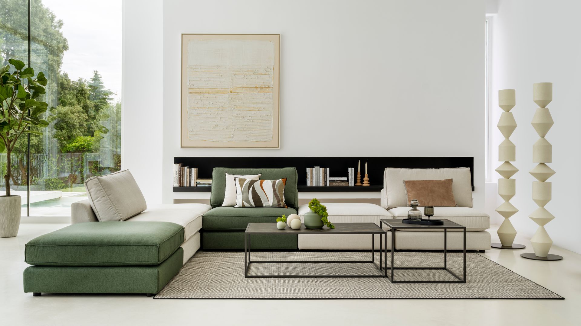Salón con sofá modular blanco y verde, mesas de centro metálicas negras, alfombra, librería baja a medida, cuadro en la pared, ventanal con vistas al jardín, esculturas de pie