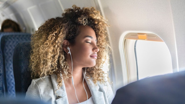 mujer con el pelo rizado dormida en un avión, con los auriculares puestos