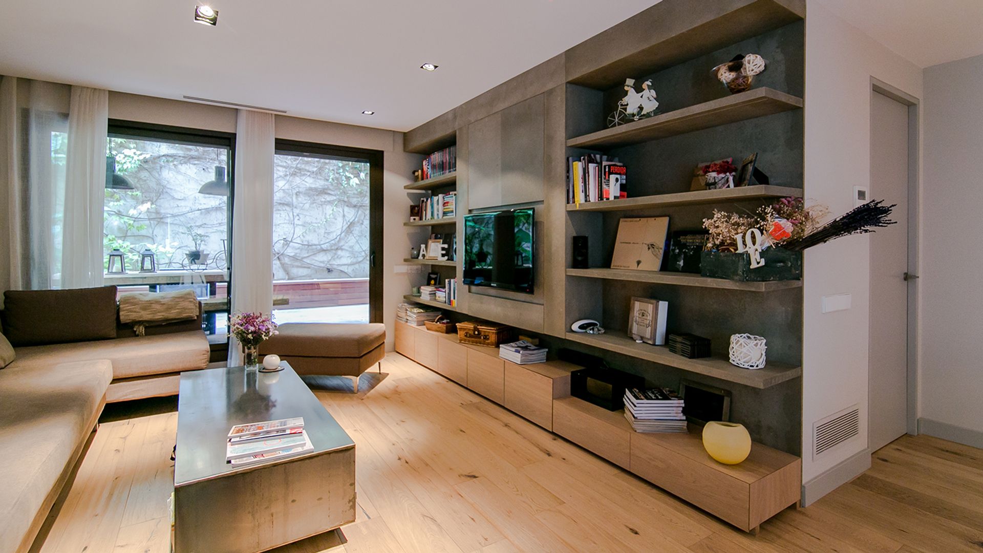 Salón con estructura con baldas y cajones con la televisión colgada, mesa de centro, suelo madera, focos techo empotrados