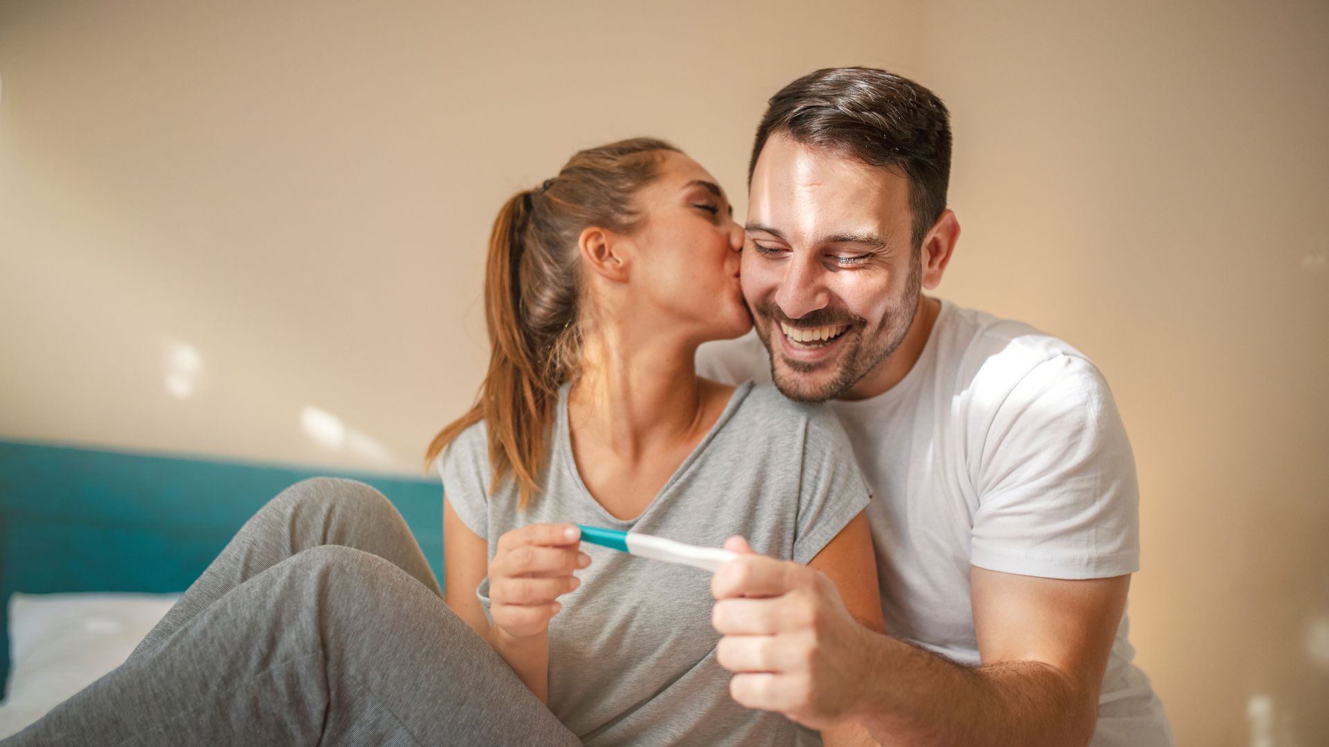 Mujer besa a su pareja al ver el resultado positivo de un test de embarazo