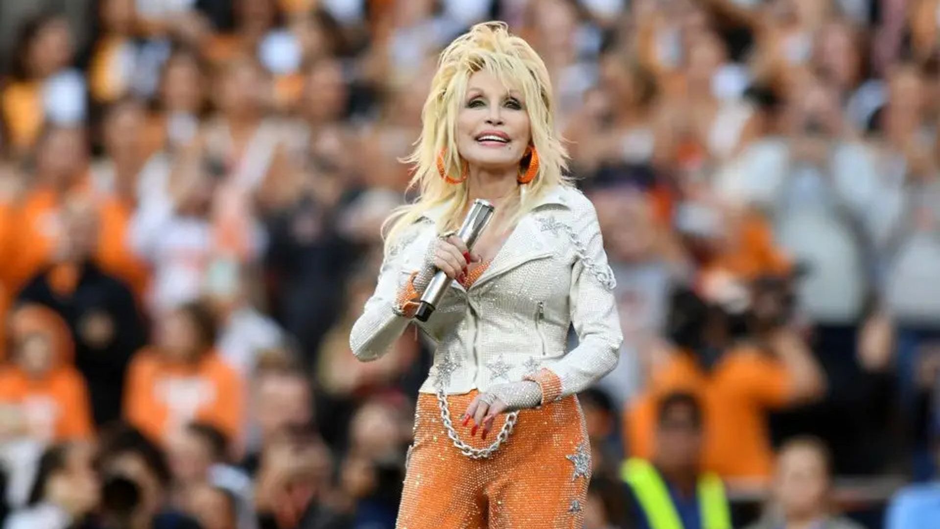 Dolly Parton aparece en el campo del Neyland Stadium vistiendo los colores naranja y blanco de los Tennessee Volunteers durante un partido de fútbol americano universitario en 2023.