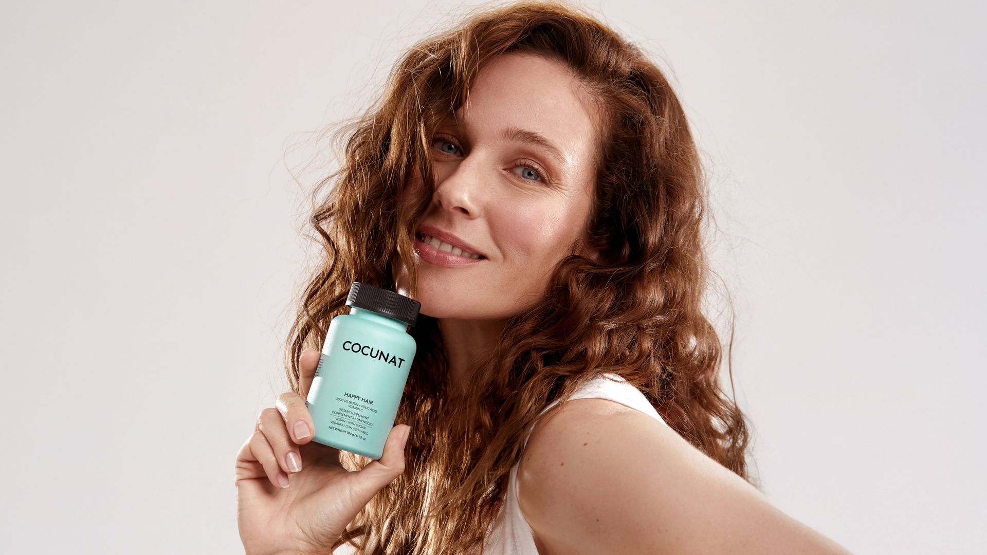 Rostro de mujer pelirroja con melena rizada con gominolas Happy Hair en la mano