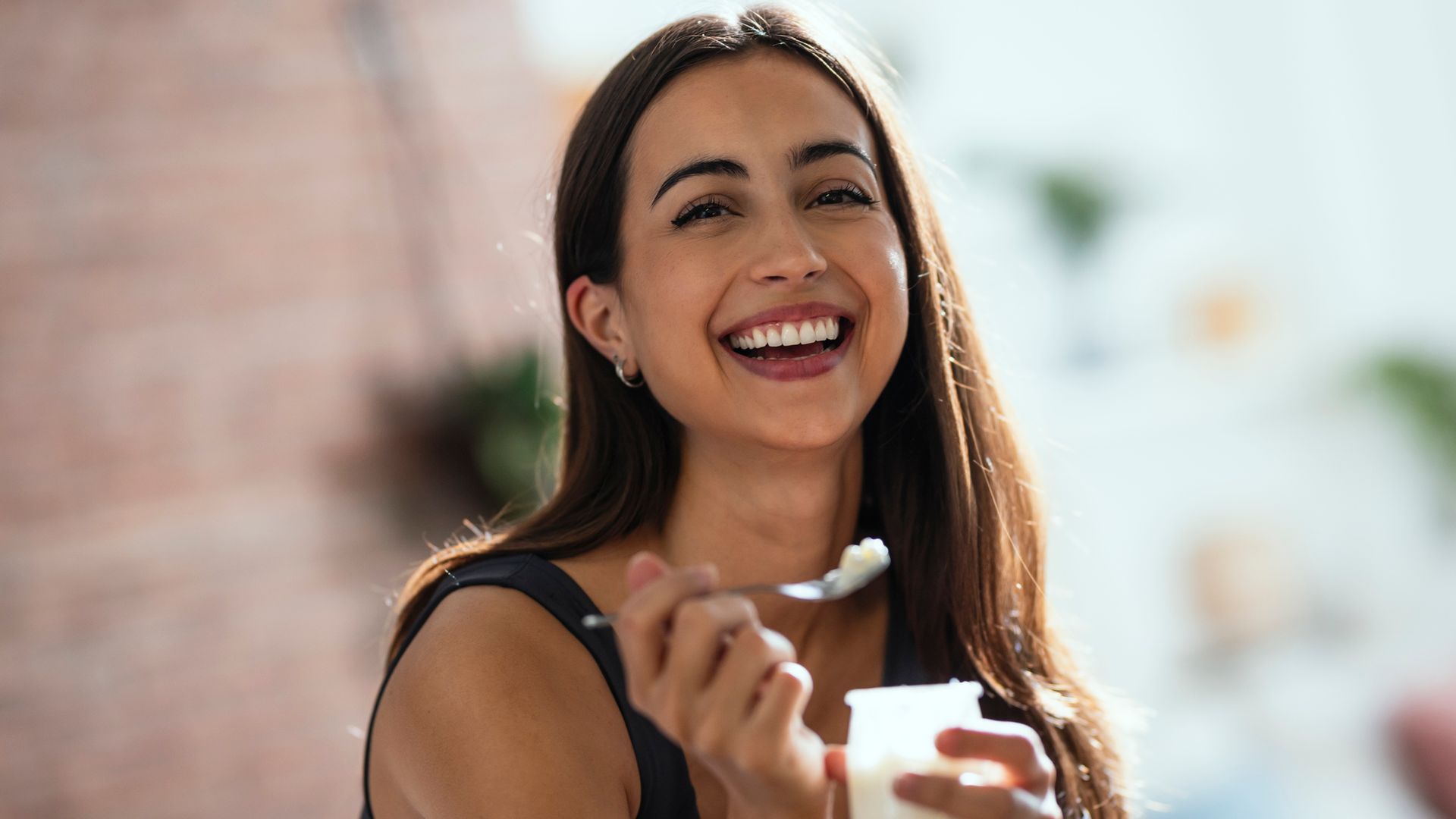 Mujer sorniendo y comiendo un yogur