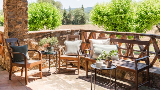 Terraza con vistas a un campo con sofá y butacas de madera, cojines y mesitas auxiliares de hierro