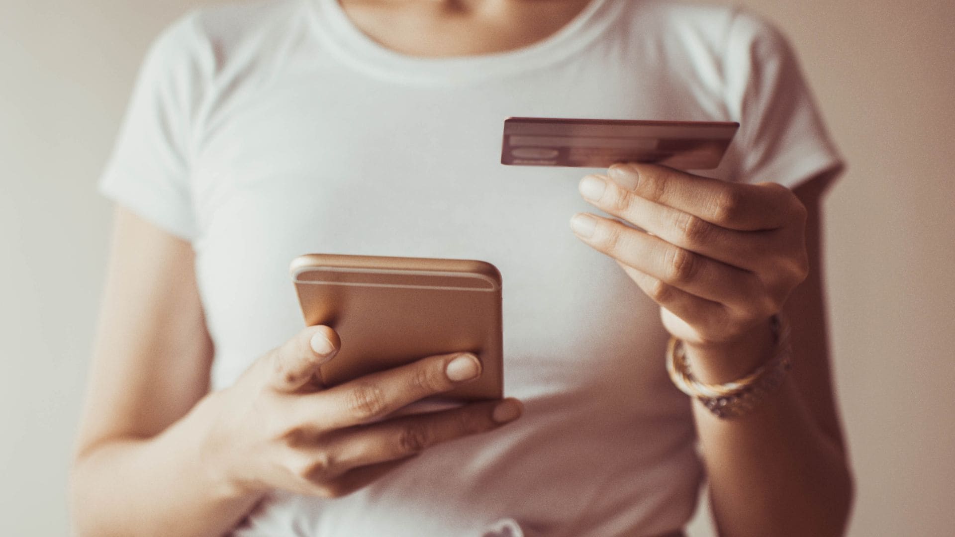 Chica comprando a través de su teléfono móvil con una tarjeta entre las manos.