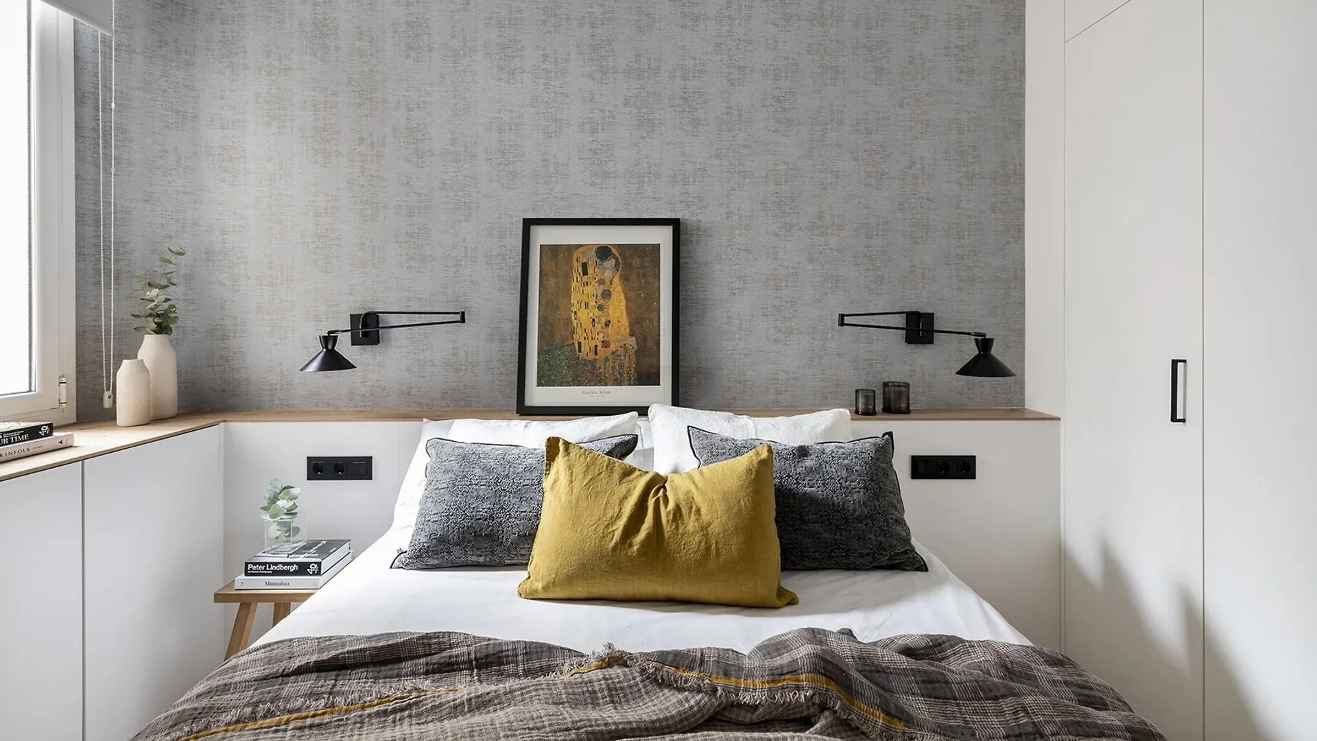 Dormitorio con papel pintado gris, cabecero a medida que integra mueble bajo la ventana, cuadro en la pared,del cabecero, apliques de pared negros a ambos lados de la cama
