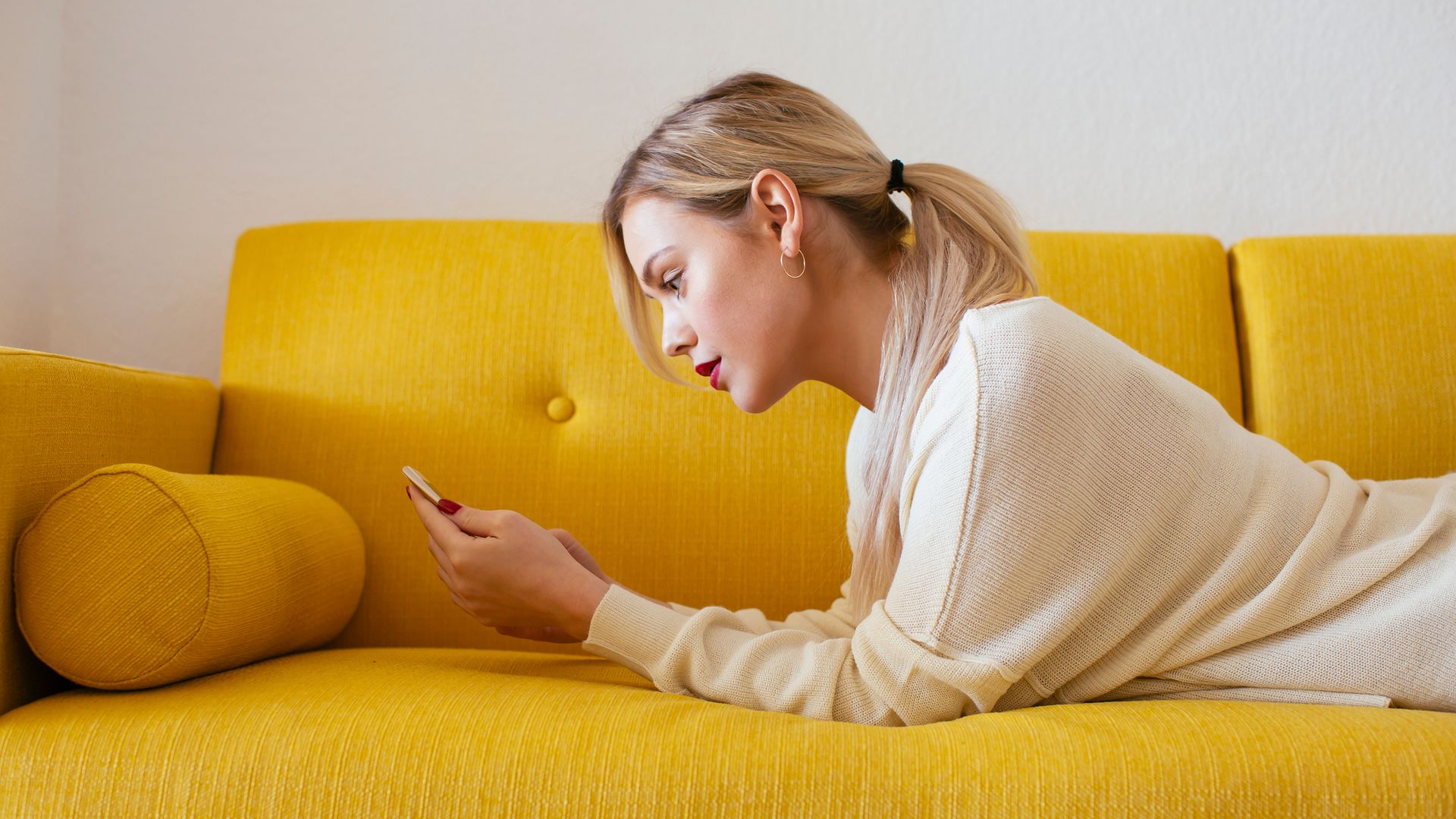 mujer joven tumbada en el sofá mirando su móvil